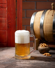 A glass of light beer on a dark table with an oak barrel next to it