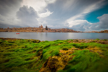 Frog view of panorama or cityscape of Valletta, capital of malta on a sunny day with storm clouds in the background. Visible long exposure water in the bay.
