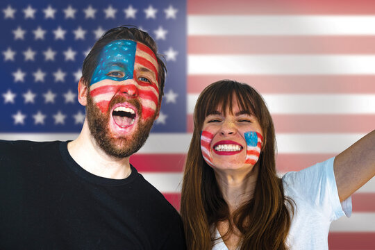 fans of the usa soccer team celebrate winning a match during the world championships; happy usa football fans with painted faces and the usa flag in the background
