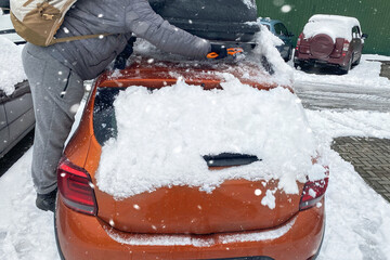 Man clears orange car from snow. Brush in mans hand. Windshield of car. Winter and snow.