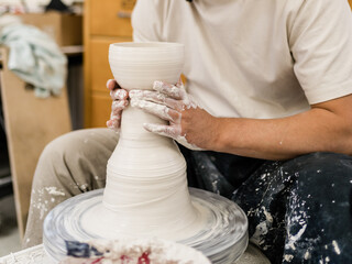 Centre clay and throw pots on the pottery wheel. Muddy work table and handmade clayware. Wet sponge. 
ceramist is smoothing molded ceramic pot.