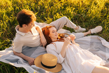 Top view of young loving woman lying of handsome man during romantic dating in green field on background of warm sunlight in summer day. Concept of love and tender relationship outdoors.