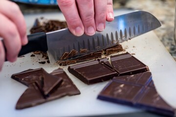 hands chopping bars of chocolate with large knife prepping to cook dessert for holiday
