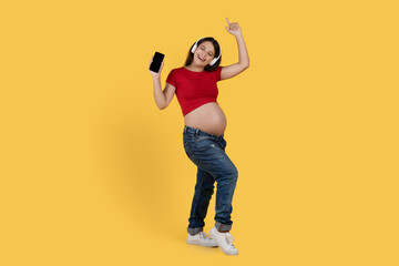 Fototapeta na wymiar Cheerful Pregnant Woman Wearing Wireless Headphones Listening Music On Smartphone And Dancing