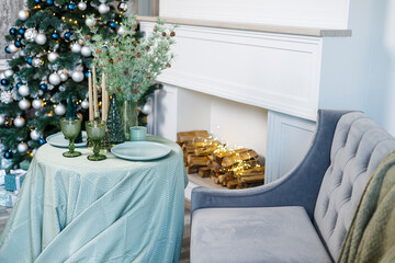 Table setting for Christmas or New Year's dinner with candles, decorations, tablecloth and napkins on the background of a Christmas tree in an apartment