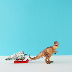 Creative composition made of dinosaur toy and sleigh with Christmas tree on blue and white...