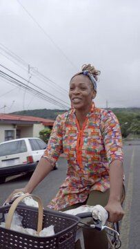 video vertical de una hermosa mujer morena con cabello afro y una pa&ntilde;oleta en su cabeza, muy sonriente vendiendo sus productos mientras se transporta en una bicicleta