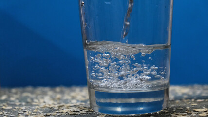 Chorro de agua cayendo en un vaso. Fondo azul