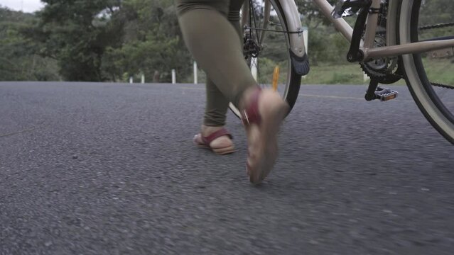 video de los pies de una mujer morena irreconocible caminando por el asfalto rodando una bicicleta 