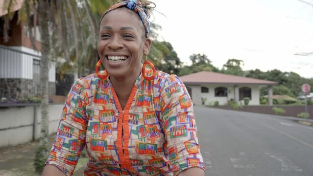 Mujer afro caribe&ntilde;a con una gran sonrisa montada en una bicicleta ofreciendo productos para la venta en la calle con ropa muy colorida
