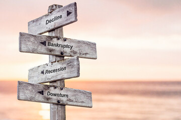 decline bankruptcy recession downturn text written on wooden signpost outdoors at the beach during sunset