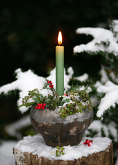 Still life with burning green candle in candle in rustic metal pot. Outdoor Christmas or winter...