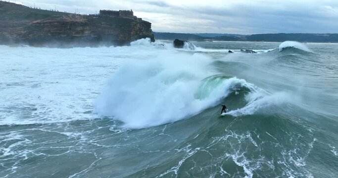 Aerial view of male surfer riding huge ocean wave in Nazare, Portugal.