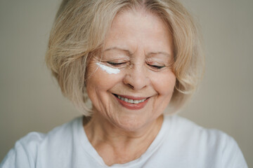 Close up portrait of senior beautiful woman applying anti-aging cream on wrinkled face. Skin care treatment concept. People lifestyle. Beauty portrait. Health
