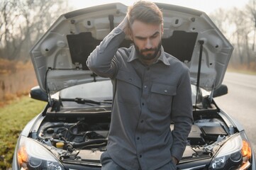 Sad driver holding his head having engine problem standing near broken car on the road. Car breakdown concept