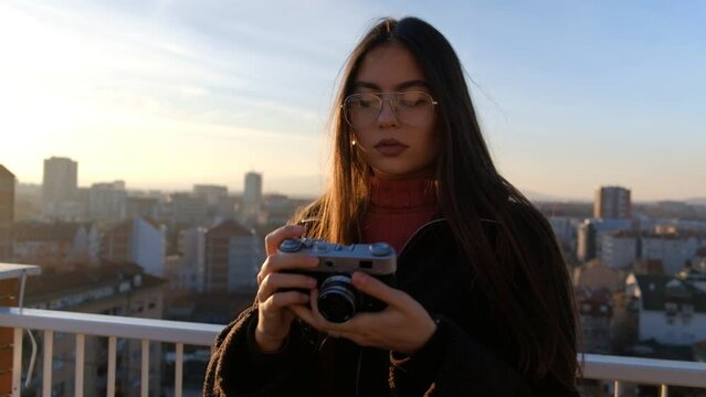 Young woman photographer taking photos with a vintage camera on a rooftop of a city building 