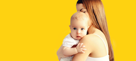 Portrait of young mother holding her cute baby on yellow background