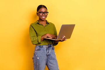 Portrait of attractive skilled cheerful girl copywriter using laptop isolated over bright yellow color background