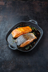 Traditional Japanese salmon fish teriyaki filet with soy souce and spinach as top view in a Nordic design pan with copy space