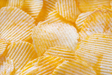Yellow crispy ridged potato chips close up. Food background, banner, header, wallpaper.