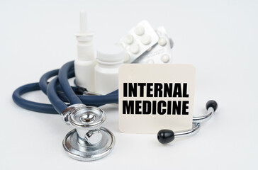 On a white surface, medicines, a stethoscope and writing paper with the text - INTERNAL MEDICINE