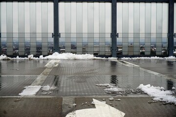Oberste Parkdecketage mit nassem Boden mit Schnee und Matsch vor transparenter Fassade und diesigem...