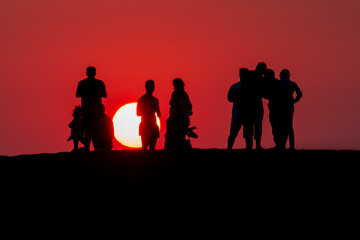 Fototapeta na wymiar few people watching the sun set on the sand