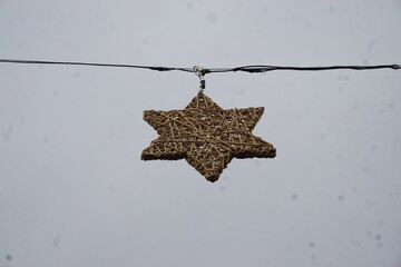 Brauner Weihnachtsstern aus Bast hängt an Seil in der Luft vor diesigem Himmel bei Regen am Mittag...