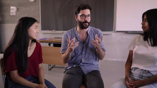 Diverse group of high school students sitting on chairs in a circle and interacting during a lesson, their Caucasian male teacher with them and talking. Education concept. High quality photo