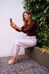 Portret of laughing girl in glases making selfie with smart phone outdoors on the city street.