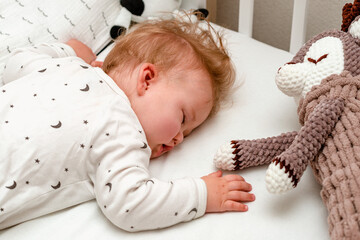baby sleeping calmly on his tummy wuth soft toy in a crib