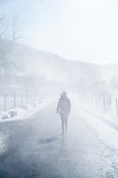 Silueta de mujer caminando por una carretera en medio de una tormenta invernal de nieve y ventisca