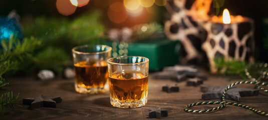 Two glasses of whiskey or bourbon with Christmas decoration on dark background. New Year, Christmas...