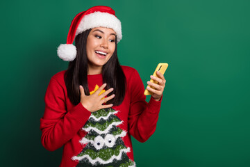 Photo of excited funny lady wear red ugly print xmas sweater cap reading apple samsung device empty space isolated green color background