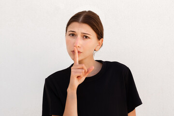 Portrait of confident young woman asking for silence over white background. Caucasian woman wearing...