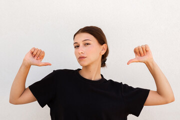 Portrait of confident young woman pointing thumbs at herself. Caucasian woman wearing black T-shirt...