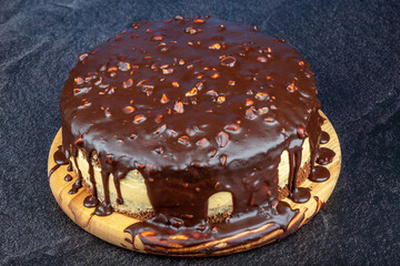 Chocolate sponge cake with almond nuts on a round cutting board.