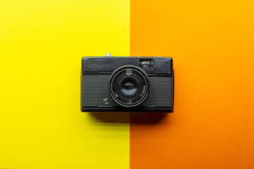 small metalic analogic camera in black colour. zenithal position. yellow and orange textured...