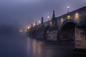 Karelsbrug van onderaf in de mist in de vroege ochtend in Praag met beelden en lantaarns op de brug. Tsjechische Republiek.