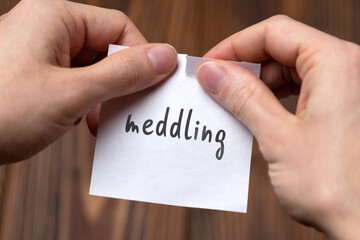 Hands of a man tearing a piece of paper with inscription meddling