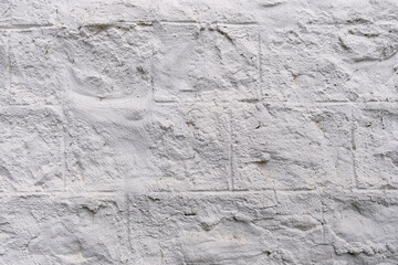 Background of white cracked plaster on the wall. An old wall with uneven cladding is full of cracks and roughness. Rough background of a white wall with bumps. Free space for text