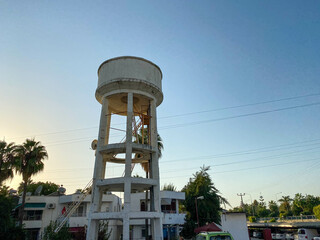 A large white water tower against the background of the sky and palm trees in a tourist warm...