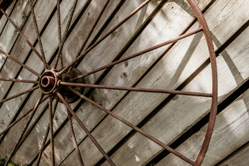 An old rusty wheel from a large cart against the background of a dilapidated unpainted fence. Abandoned place of rural type with a rusty wagon wheel close-up