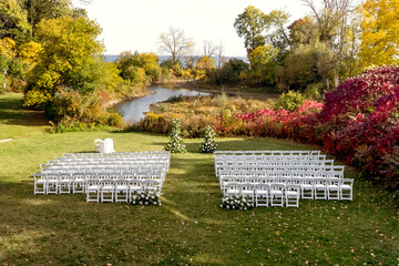 Wedding ceremony with white chairs for guests and an arch on a green lawn with a lake in the background. Traditional ceremony in the form of a wedding ceremony. Wedding decorations without guests
