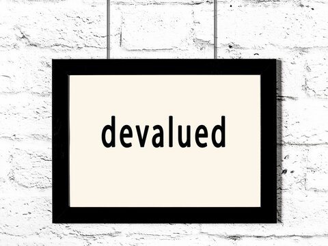 Black frame hanging on white brick wall with inscription devalued