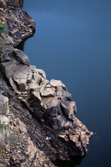 Sharp boulders bordering a dark blue lake.The rocks as if cut down towards the water and continue under the water. The water is bluish grey, creating a feeling of stress, unhappiness and fear.