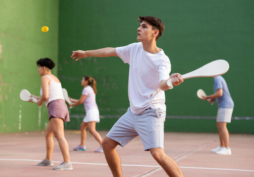 Young male pelota player hitting ball with wooden racket during training game on outdoor Basque pelota fronton.
