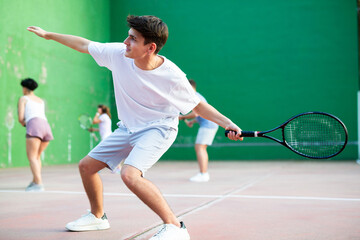 Active young man with racket playing frontenis game on outdoor court