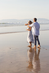 Lively male and female couple spending time at beach. Husband and wife in casual clothes hugging...