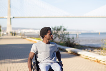Happy Black man in wheelchair enjoying sea view while riding along park road near seashore. Smiling...